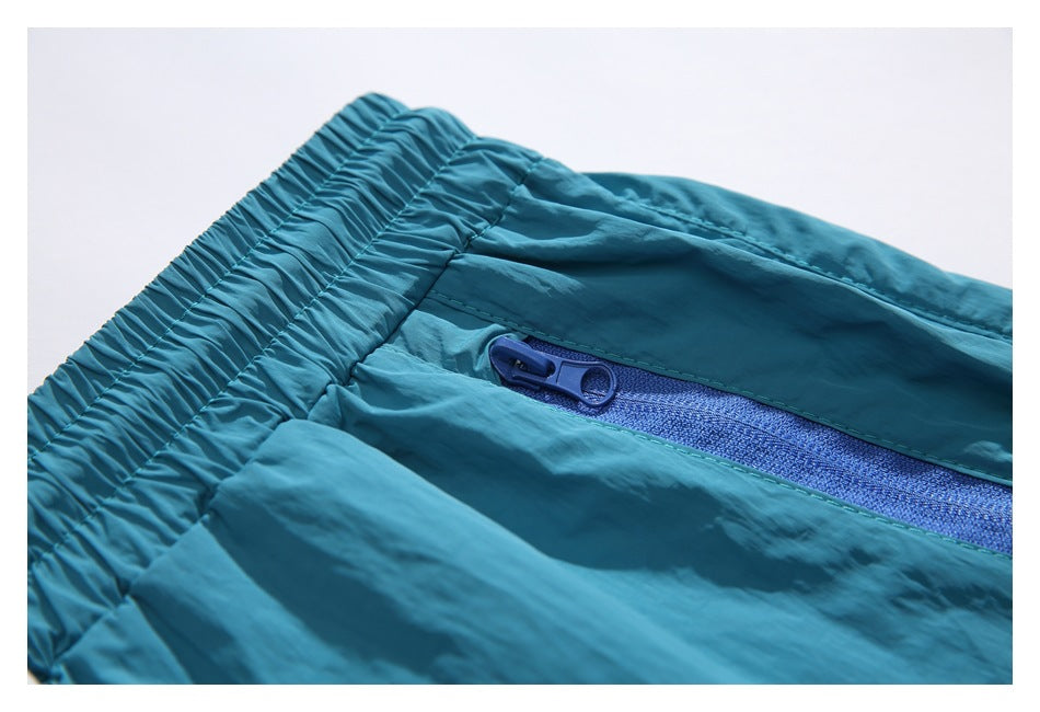 Close-up of the teal shorts' elastic waistband and blue zipper with a ring-shaped pull.