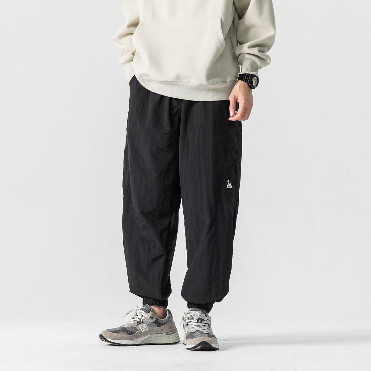 Front view of a model wearing black loose jogger pants with elastic cuffs and a small white emblem.