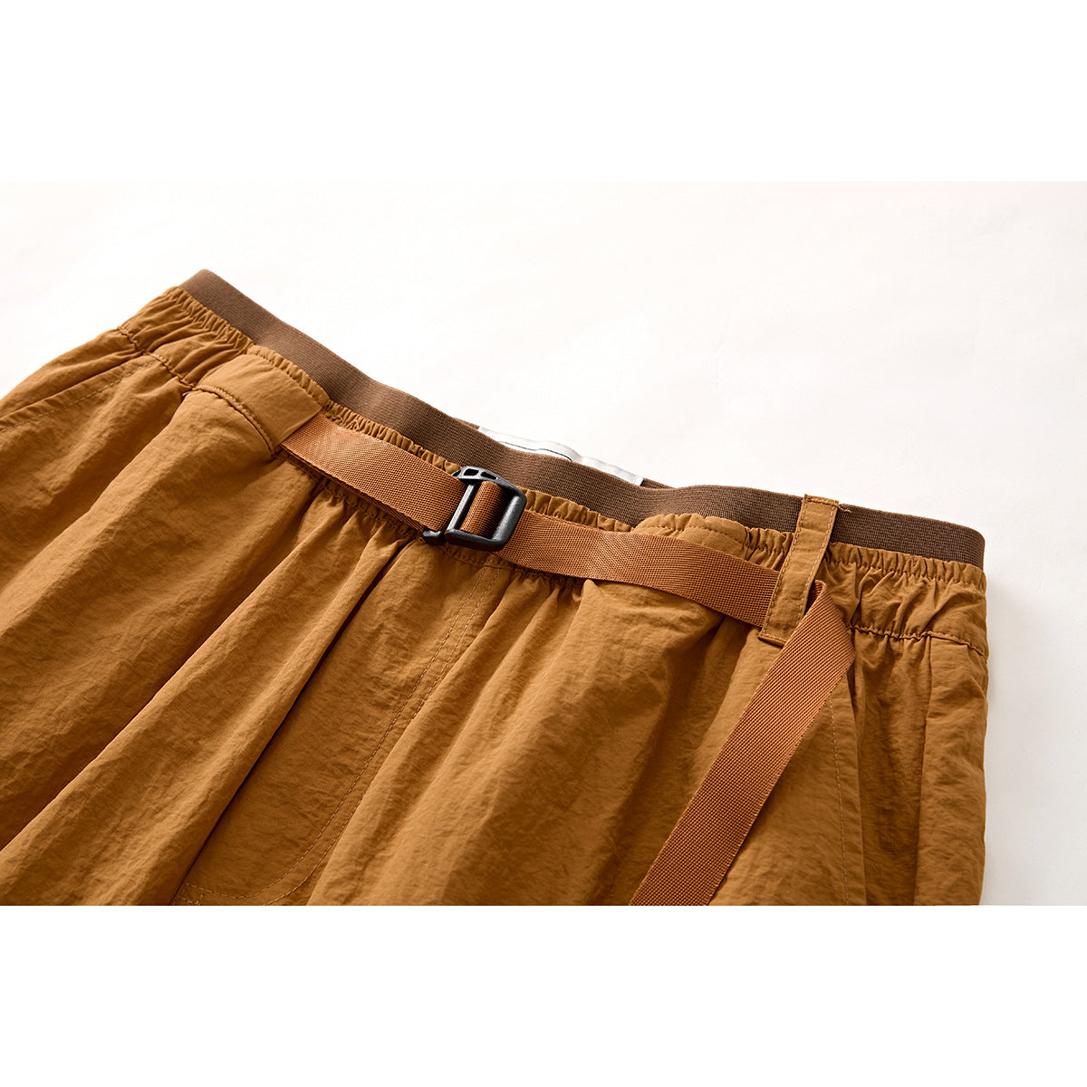 Close-up of ochre shorts showing the elastic waistband and adjustable webbing belt with a black buckle.