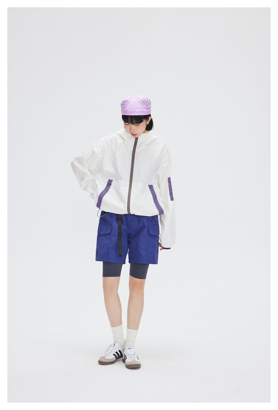 Model wearing a white hooded jacket with purple accents and blue cargo shorts.