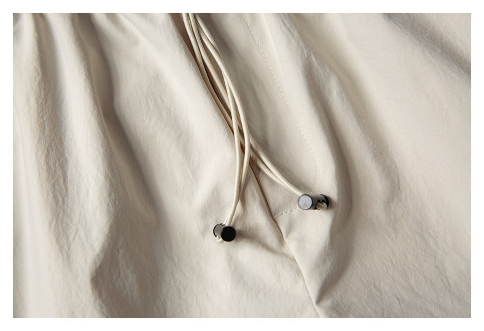 Close-up of the light beige shorts' drawstrings with black-and-silver cord ends.