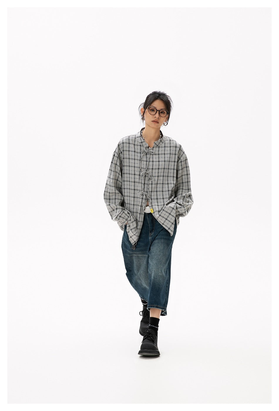 Model wearing a gray plaid tie-front shirt open over a white top with wide-leg blue jeans and black boots