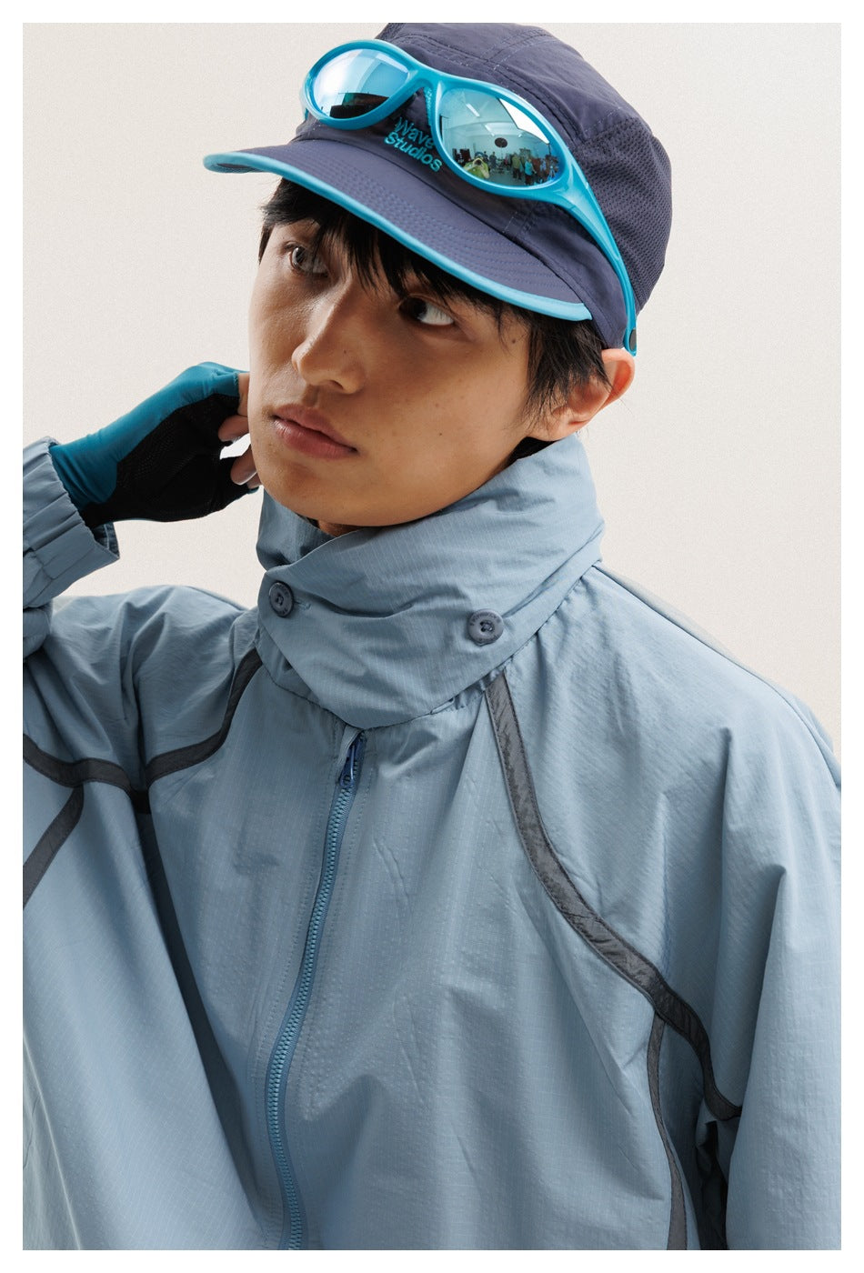 Close-up of a pale blue jacket's high buttoned collar, zipper and dark trim, worn by a model.