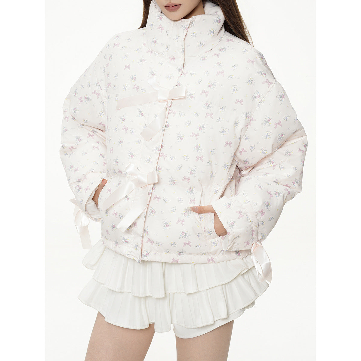 Close view of an ivory floral-print puffer jacket with ribbon ties, worn with a white layered ruffle skirt.