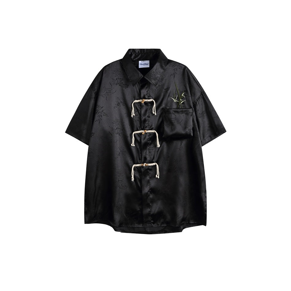 Black short-sleeve satin-look jacquard shirt with three cream rope loop closures and a bamboo-embroidered chest pocket