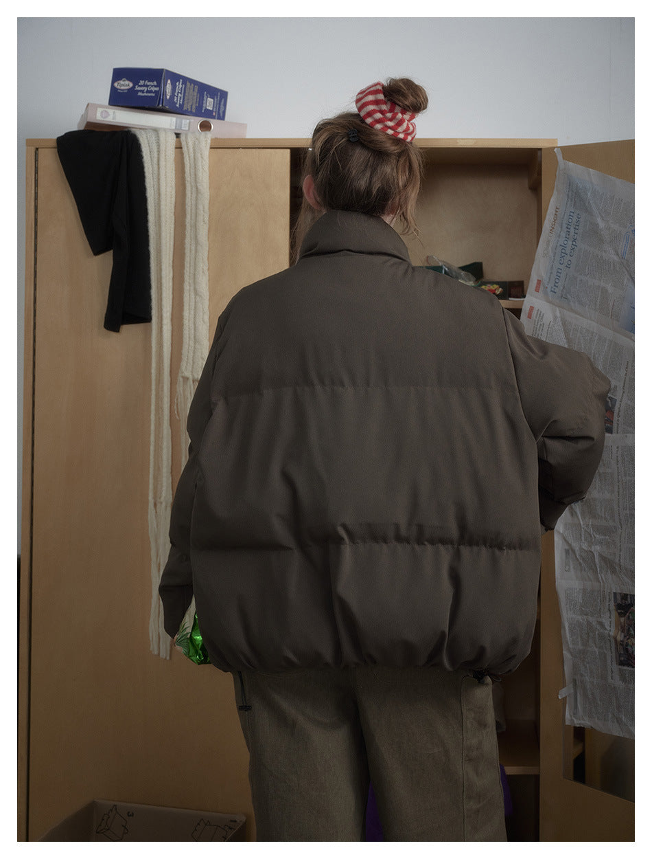 Back view of a model wearing an oversized dark brown puffer jacket with a high collar and horizontal quilting.
