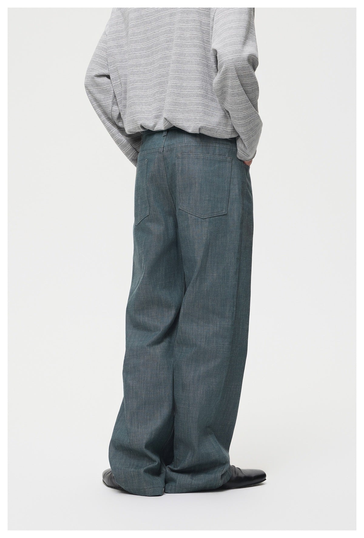 Rear view of a model wearing loose blue-gray trousers with two back pockets and a gray striped top.