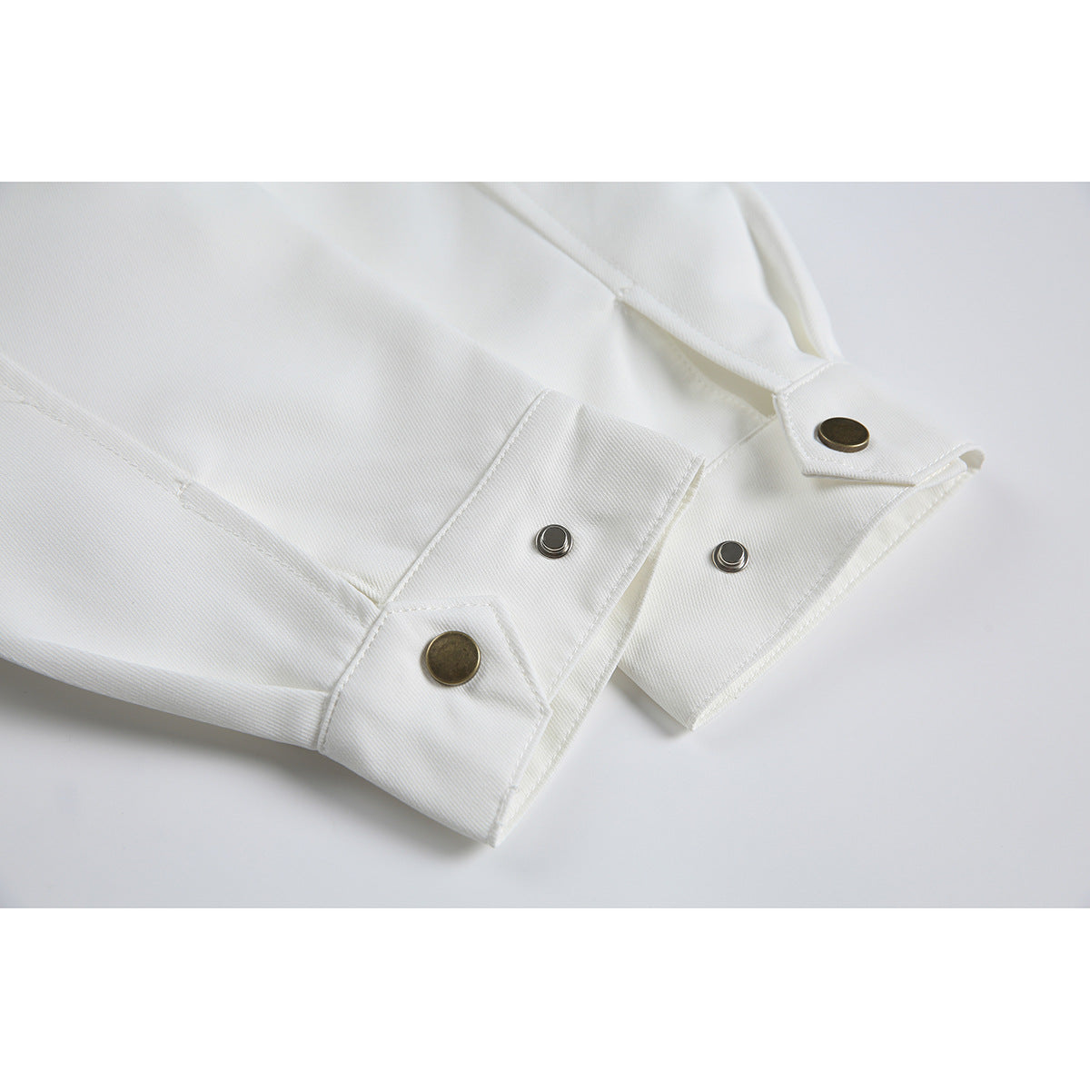 Close-up of white garment cuffs with antique-brass buttons and metal snaps.