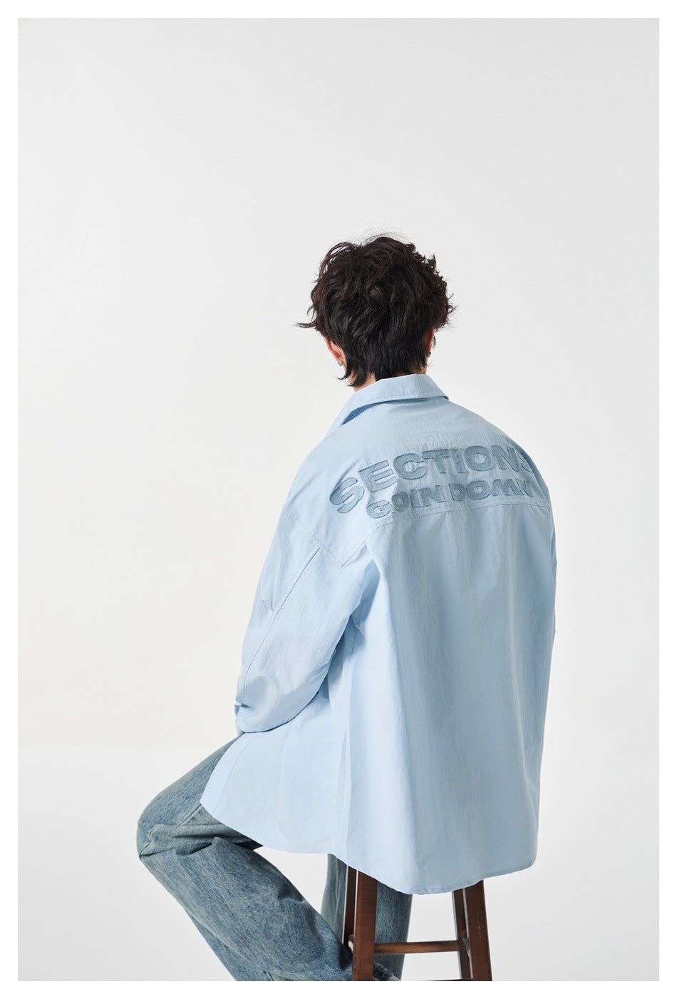 Back view of a pale blue shirt with large tonal embroidered lettering across the shoulders.