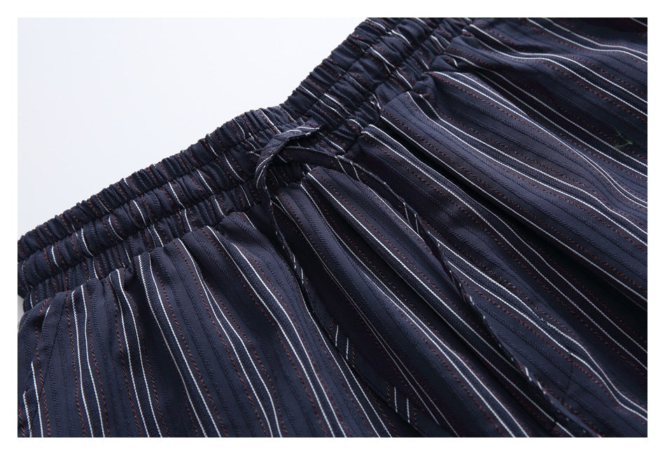 Close-up of a dark navy garment with an elastic waistband, drawstring, and fine white and muted red stripes.