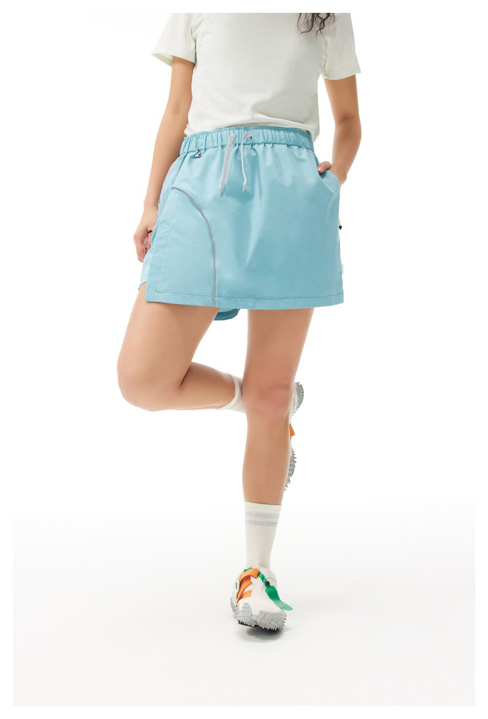 Front view of a model wearing a light blue drawstring athletic skirt with curved pocket seams.