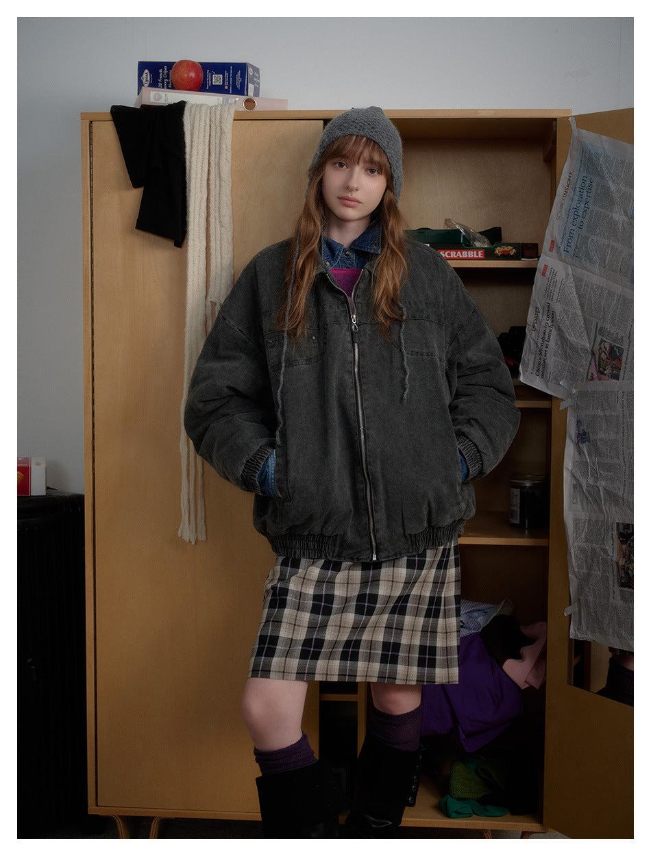 Full-length model wearing a charcoal zip-up jacket with elastic trim, paired with a plaid skirt and black boots.