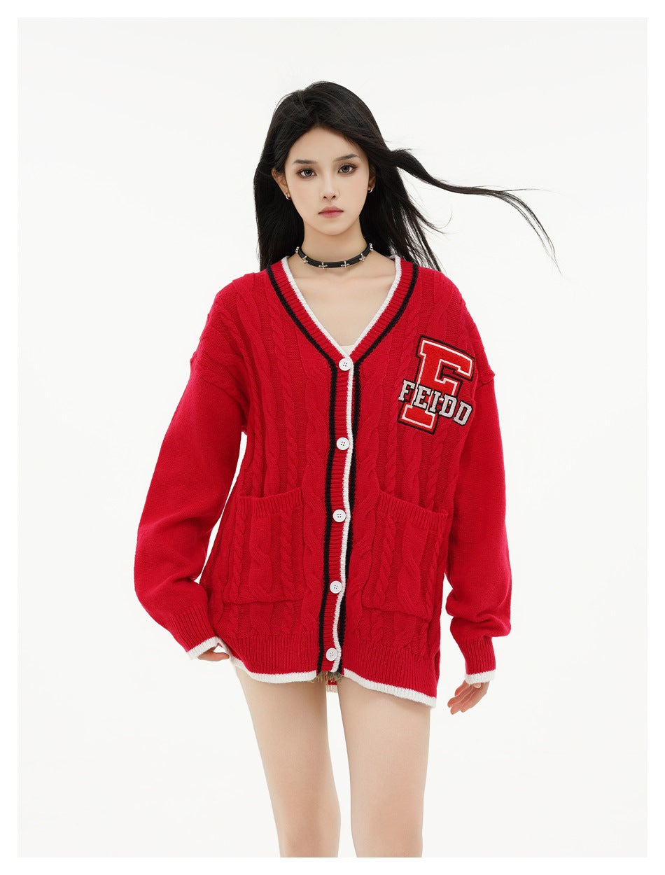 Front view of a model in a red cable-knit cardigan with white buttons, striped trim, patch pockets and a letter patch.