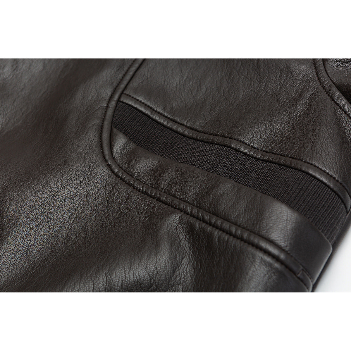 Close-up of dark brown jacket fabric and a ribbed cuff inset framed by curved piping.