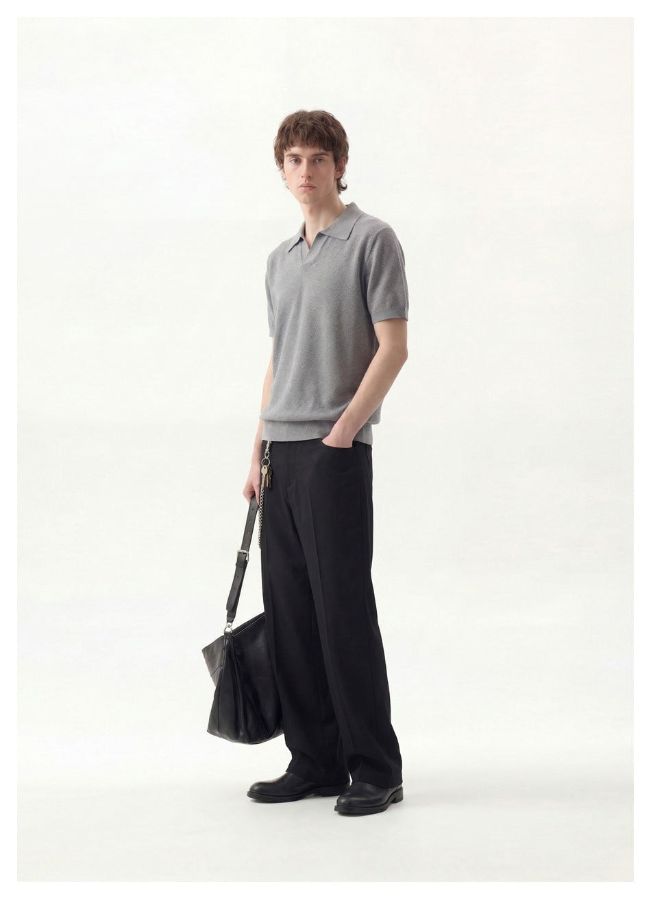 Full-length model wearing a gray short-sleeve collared polo and loose black trousers, carrying a black bag.