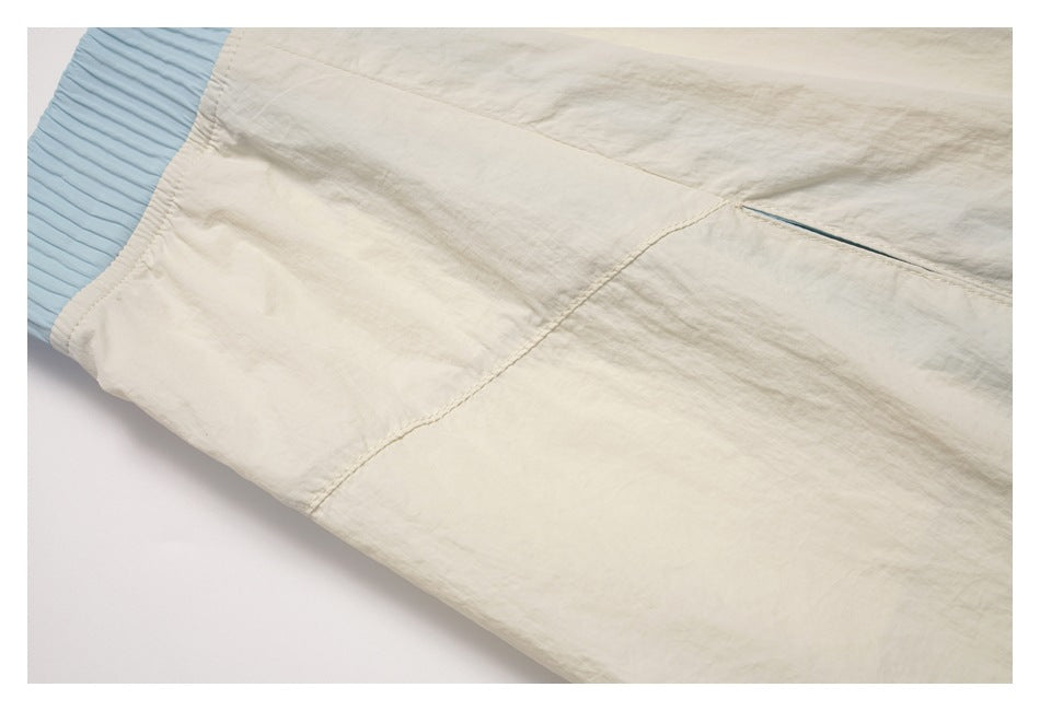 Close-up of cream garment fabric with a curved stitched seam beside a pale blue ribbed elastic edge.