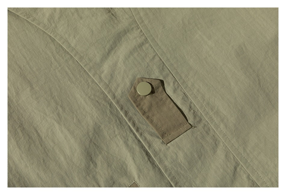 Close-up of olive ripstop-like jacket fabric and a small snap-fastened tab.