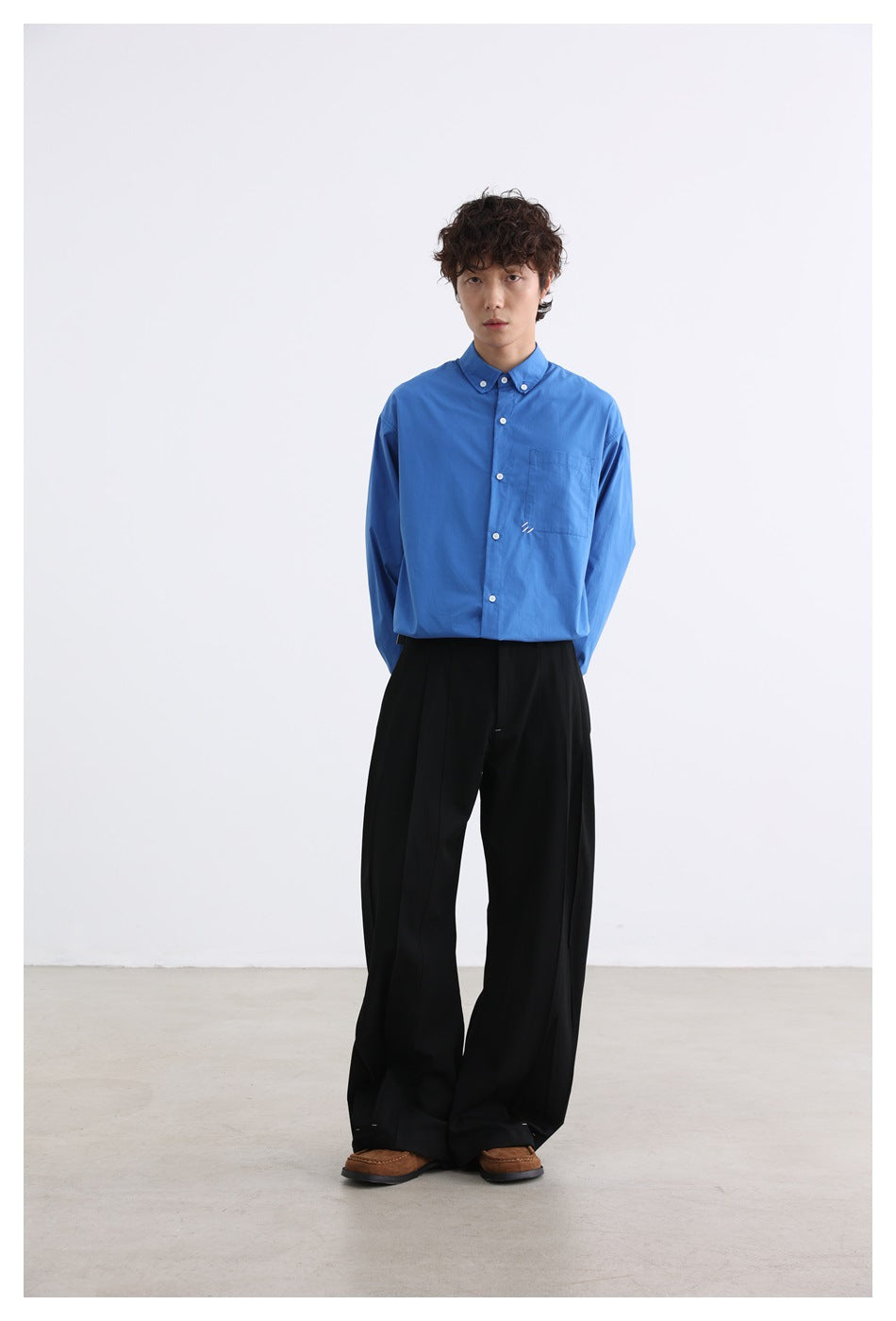 Full-length front view of a model wearing a bright blue button-down shirt, black wide-leg trousers, and brown shoes.