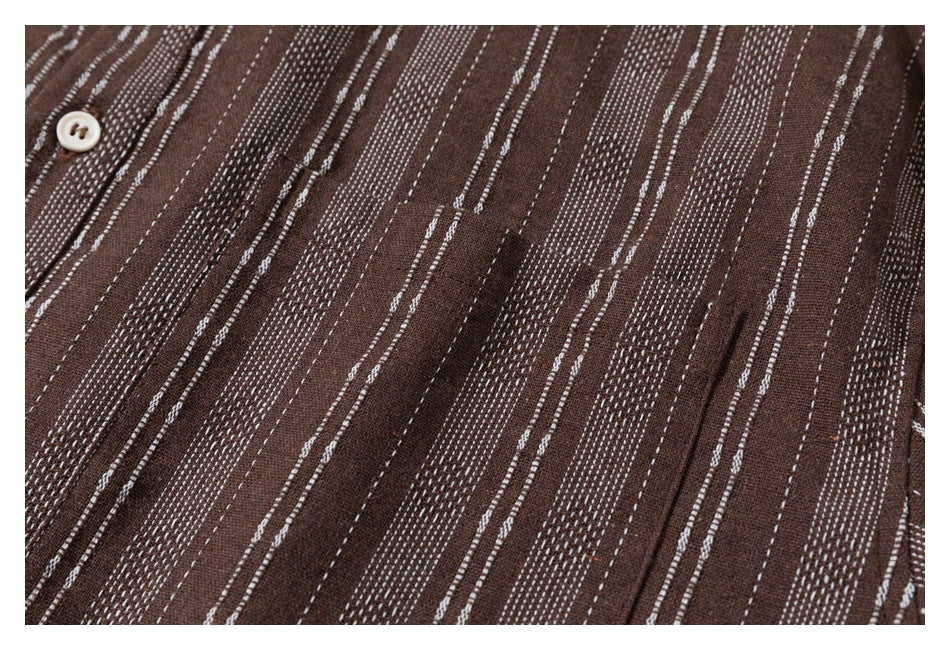 Close-up of a brown shirt's chest pocket and cream button against irregular white stripes.