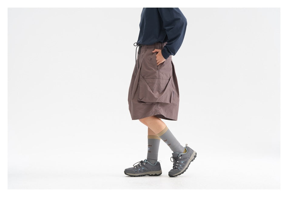Cropped view of a person wearing mauve cargo shorts with oversized pockets, a navy top, gray socks, and hiking shoes.