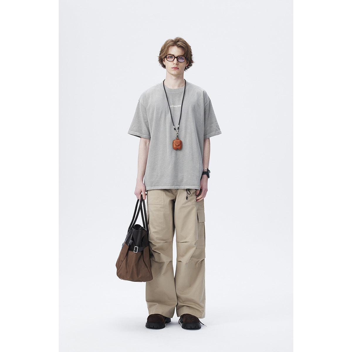 Model wearing an oversized light gray T-shirt with small chest text and beige cargo pants, shown full length.