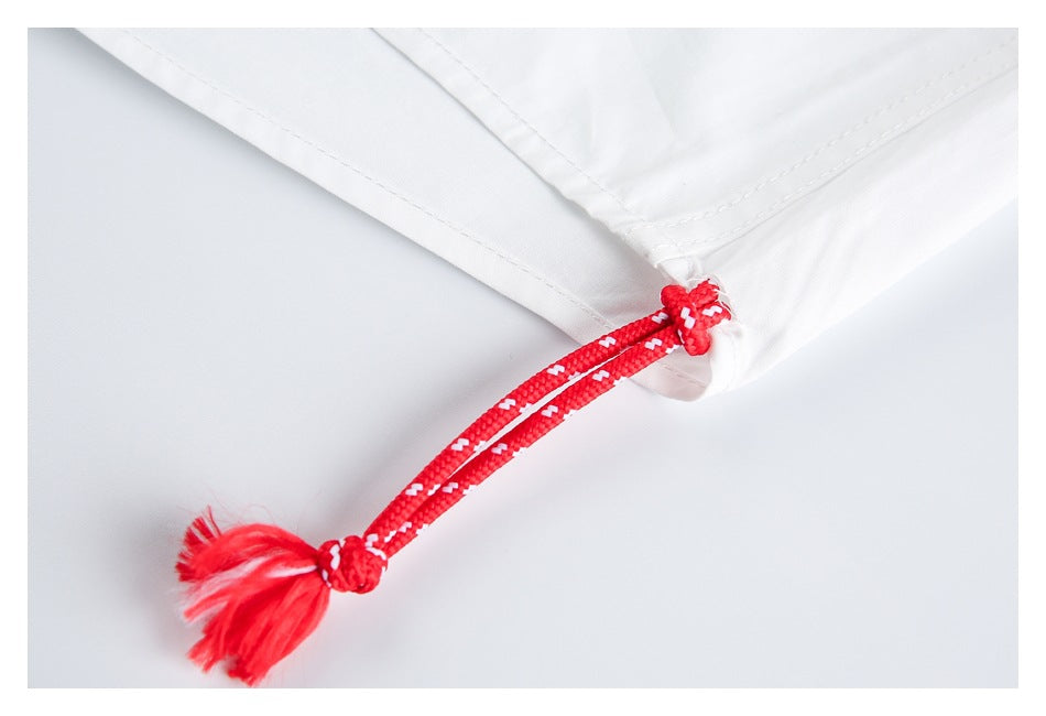 Close-up of a red-and-white braided drawstring with a tassel attached to a white garment hem.