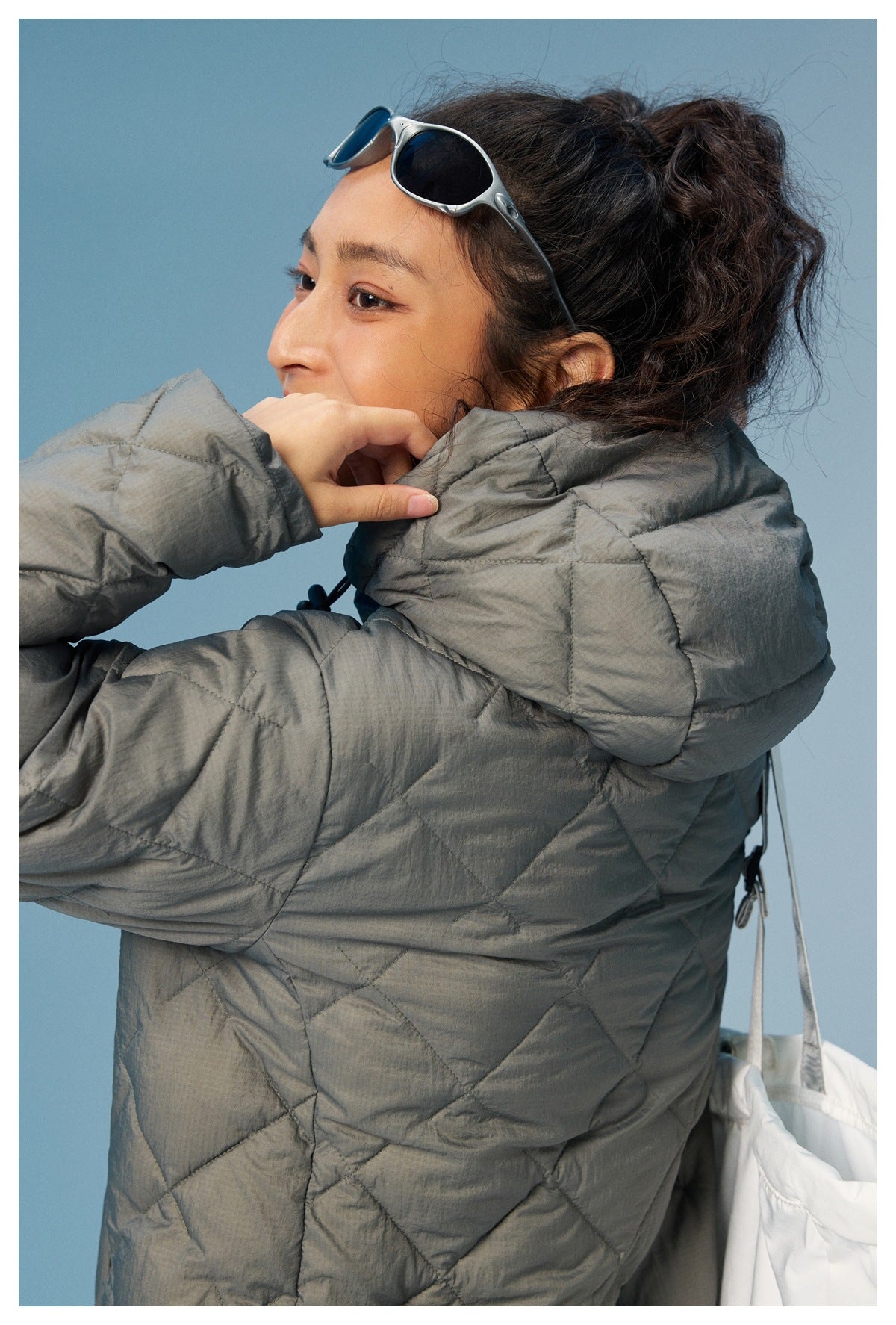 Close side view of a model wearing the gray quilted coat, showing its padded hood and back quilting.