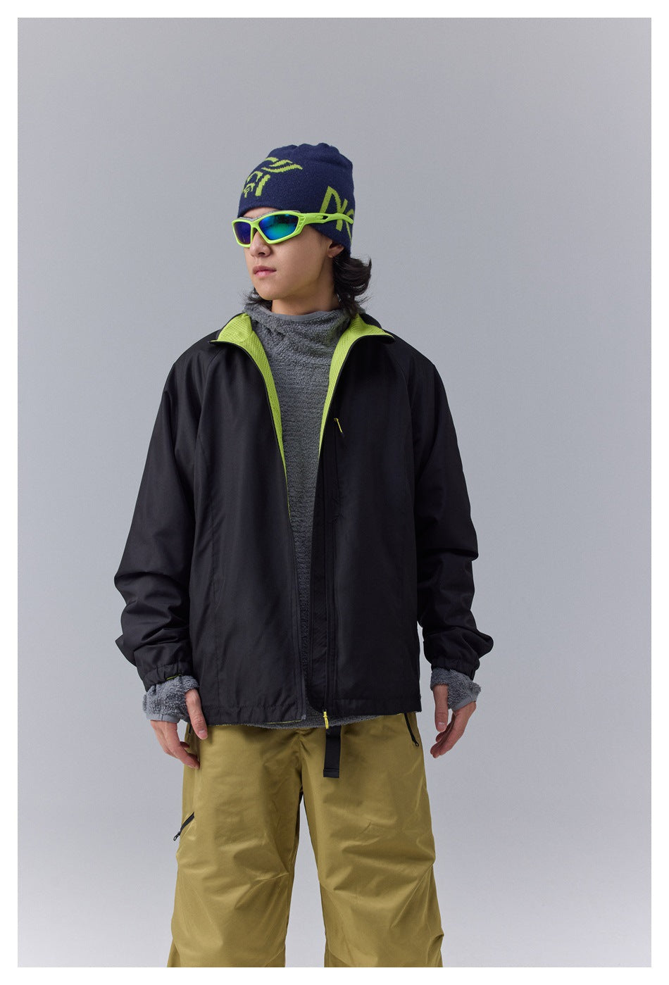 Model wearing a black zip jacket with lime lining, gray fleece layer, and olive pants, shown from the front.