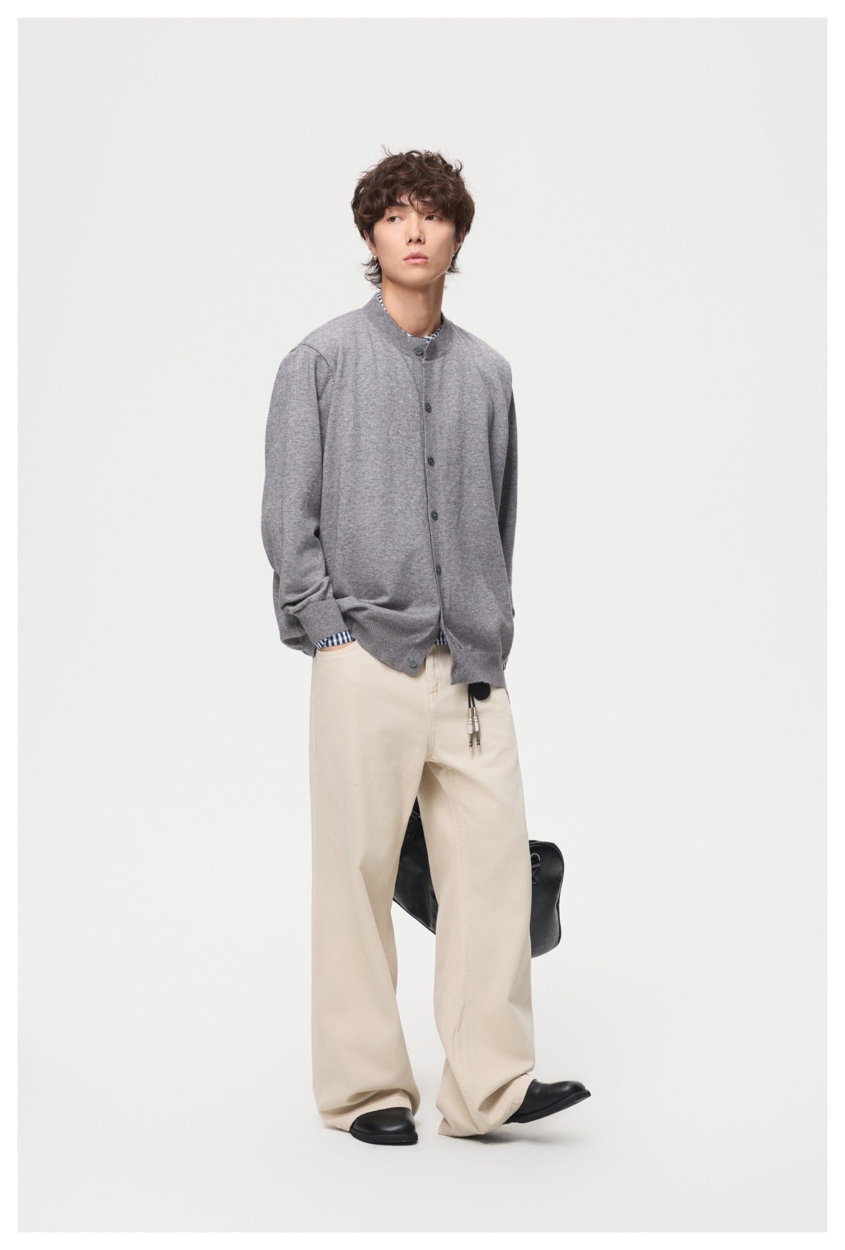 Model wearing a gray button-front cardigan with a stand collar over a checked shirt and cream trousers.