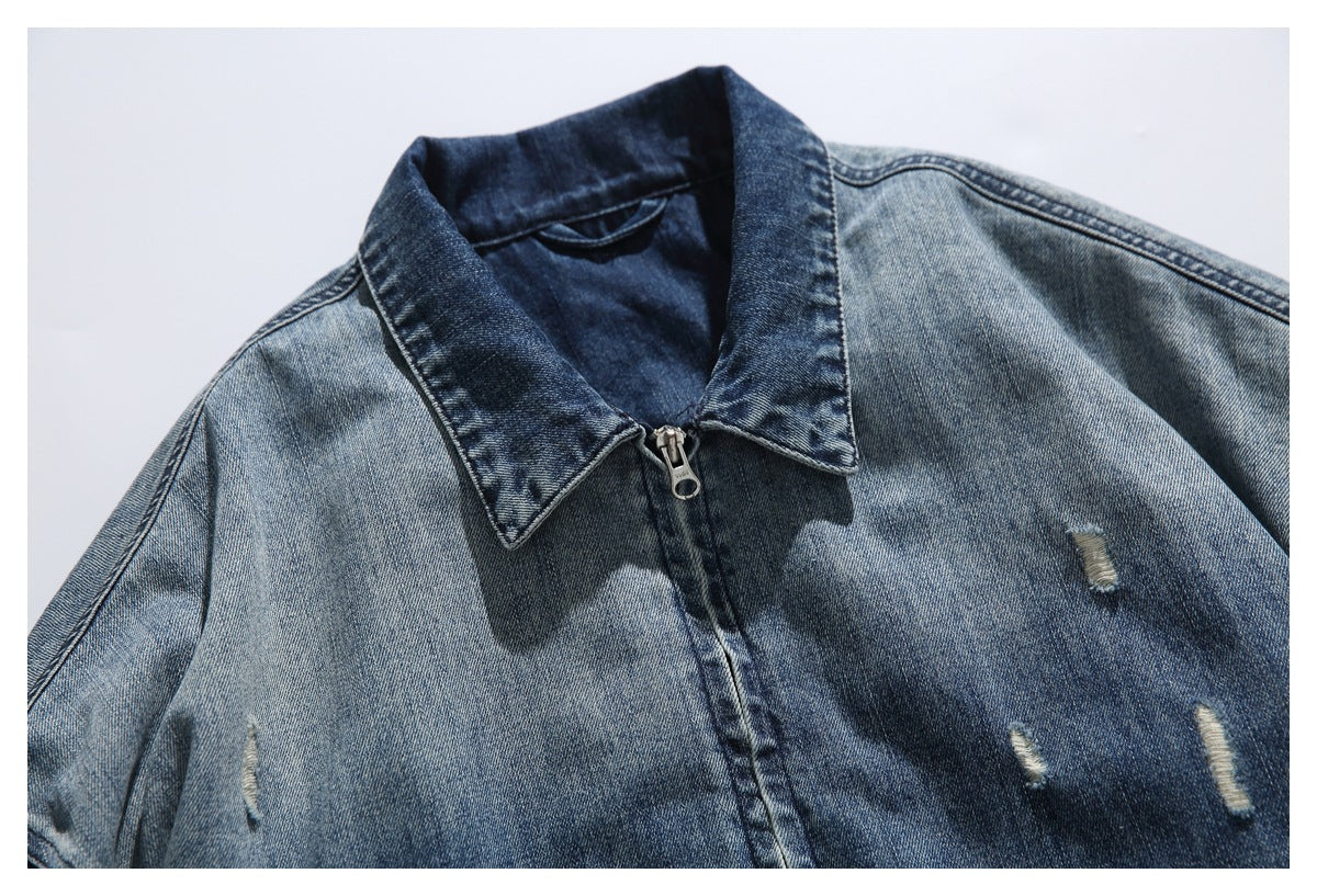 Close-up of a blue distressed denim jacket showing its pointed collar, front zipper and small frayed tears.