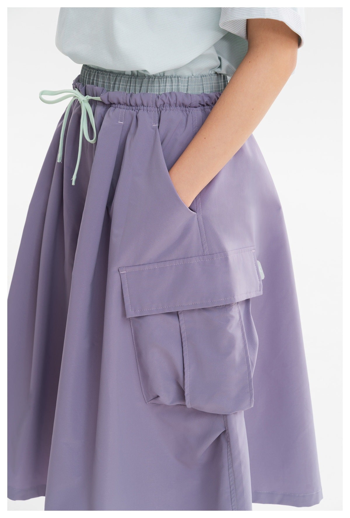 Close-up of a lavender cargo skirt showing its elastic waist, mint drawstring, and large flap pocket.