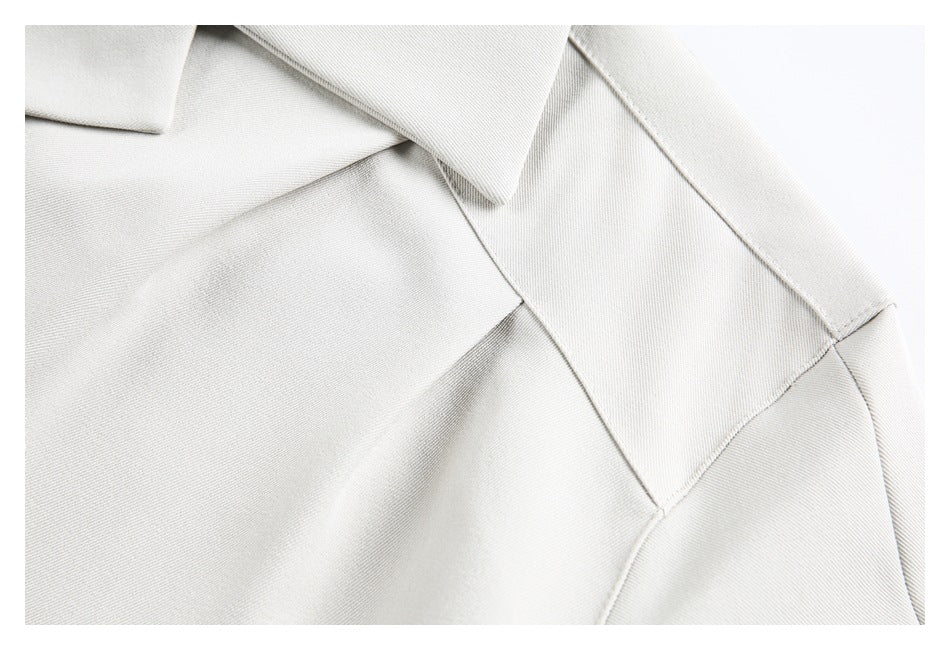 Close-up of a light ivory garment's pointed collar and stitched shoulder seam.