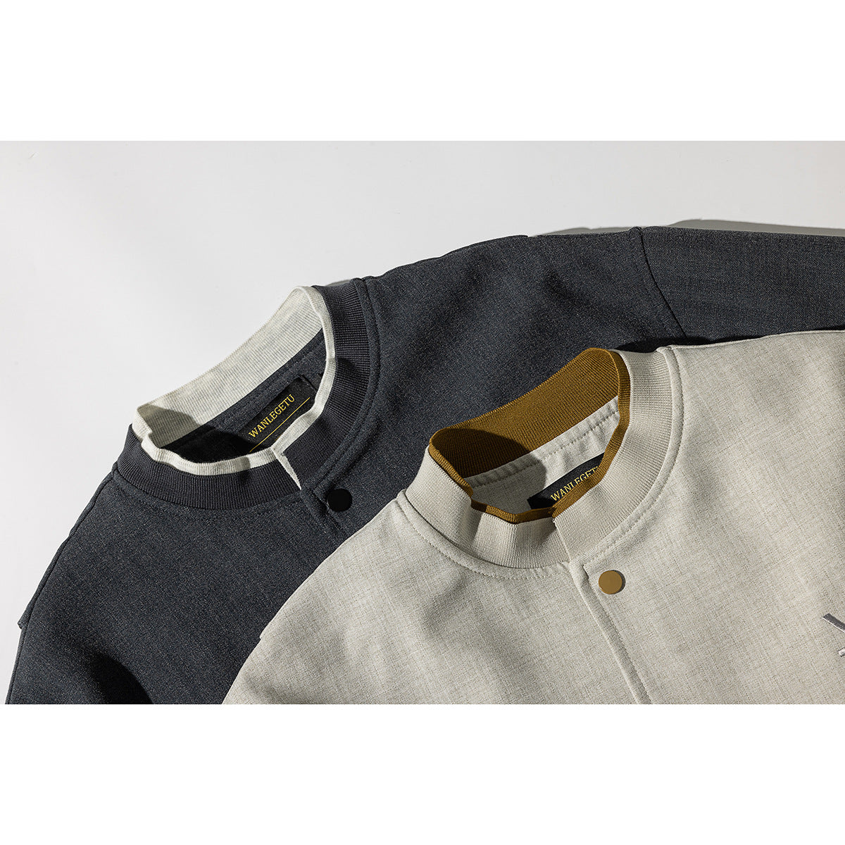 Close-up of light beige and charcoal jackets showing ribbed collars, contrasting inner trim, and snap-button plackets.