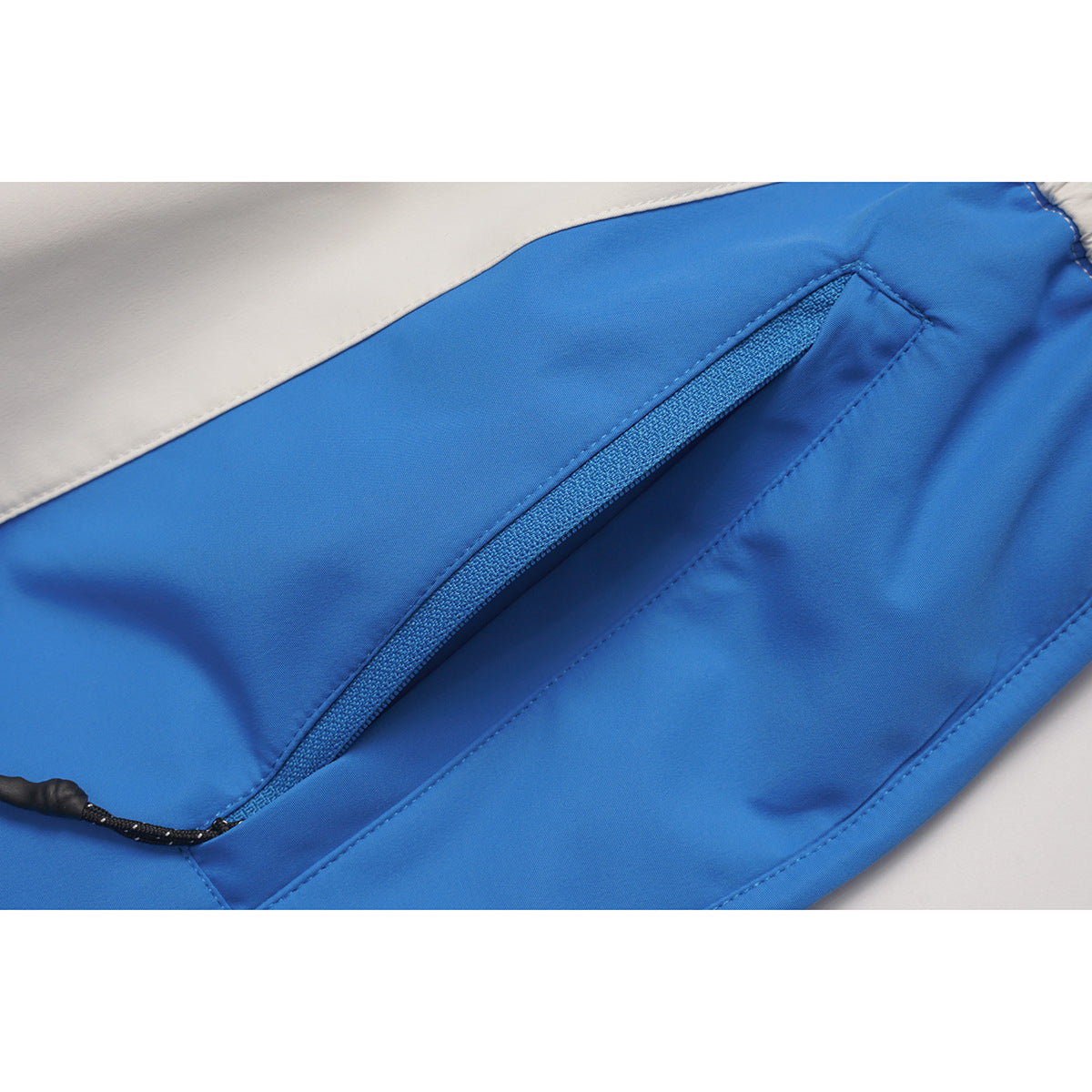 Close-up of a blue pants pocket with a diagonal zipper and black pull against a white panel.