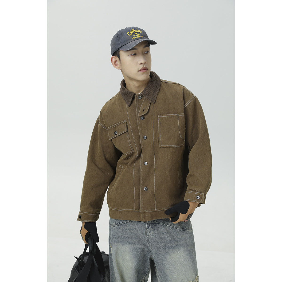 Model wearing a brown work jacket with contrast stitching, a corduroy collar, and two chest pockets.