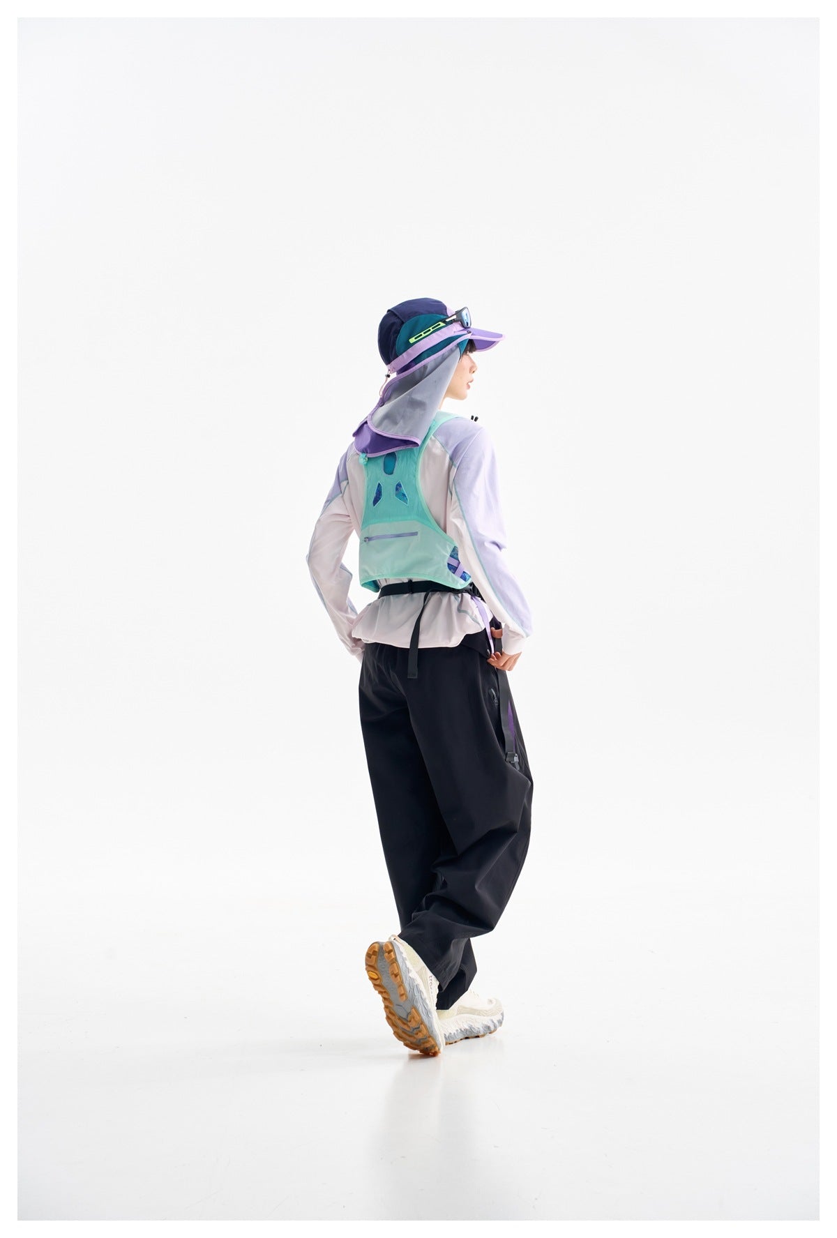 Model in a rear three-quarter view wearing a mint hiking vest, pale lavender top and black trousers.