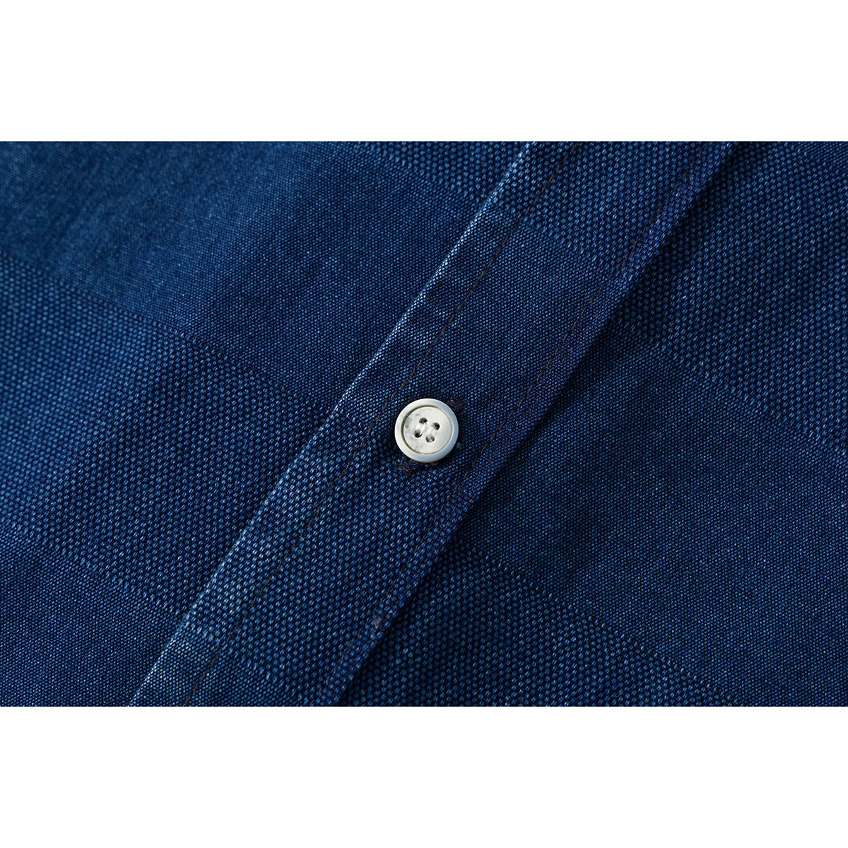 Close-up of a pale button on the navy shirt's textured, subtly striped fabric.