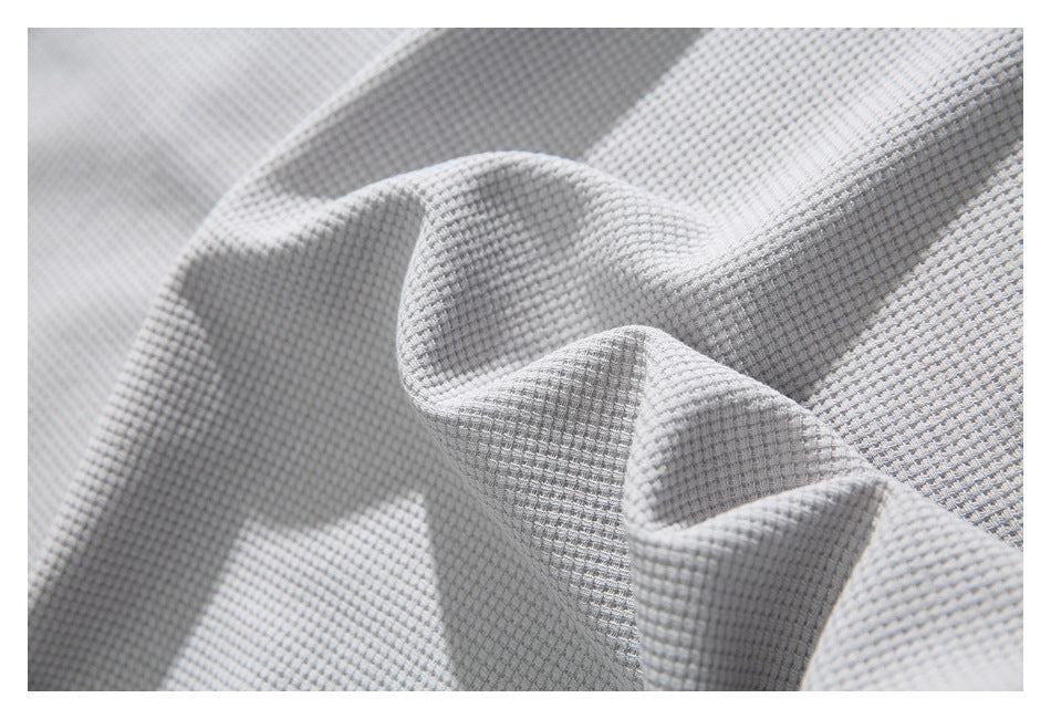 Macro view of the raised waffle texture of light gray shirt fabric draped into soft folds.