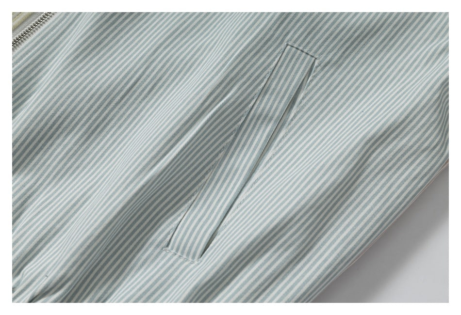 Close-up of blue-gray and white striped fabric with a diagonal pocket seam and zipper teeth at the upper left.
