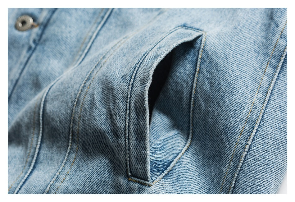 Close-up of a curved pocket opening on a light blue denim jacket.