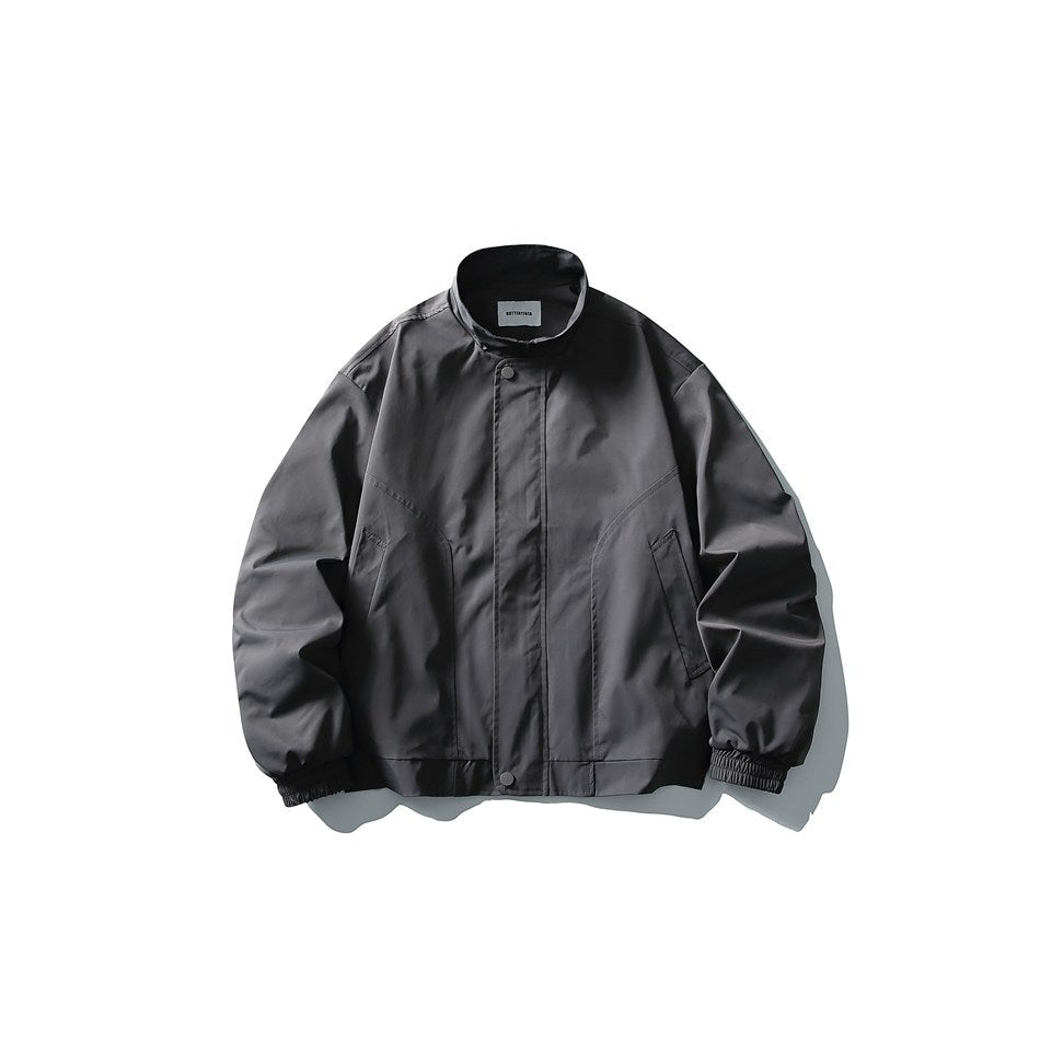 Dark gray stand-collar jacket with snap placket, slanted front seams and elastic cuffs, flat lay on white