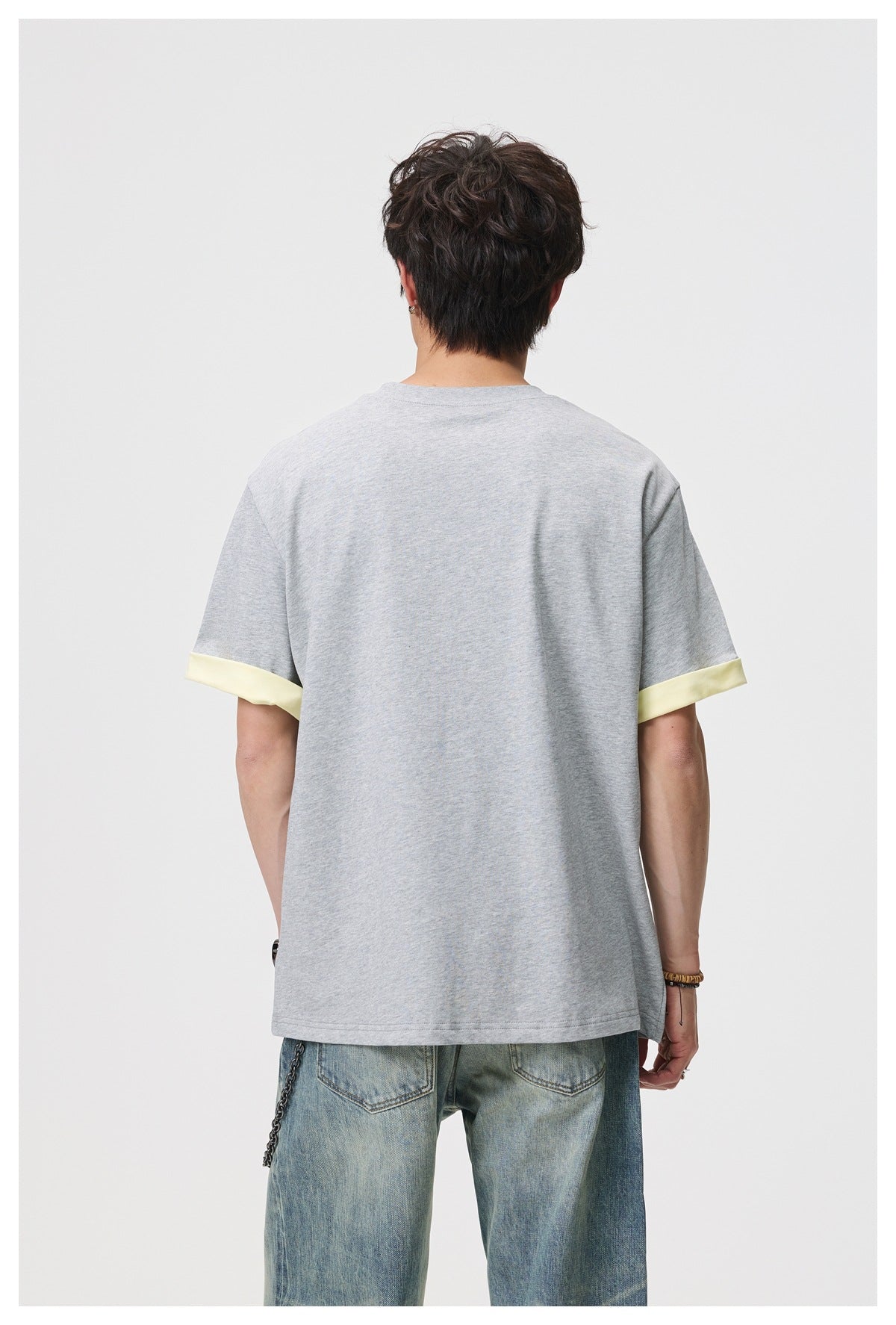 Back view of a man wearing a gray short-sleeve T-shirt with yellow cuffs and light-wash jeans