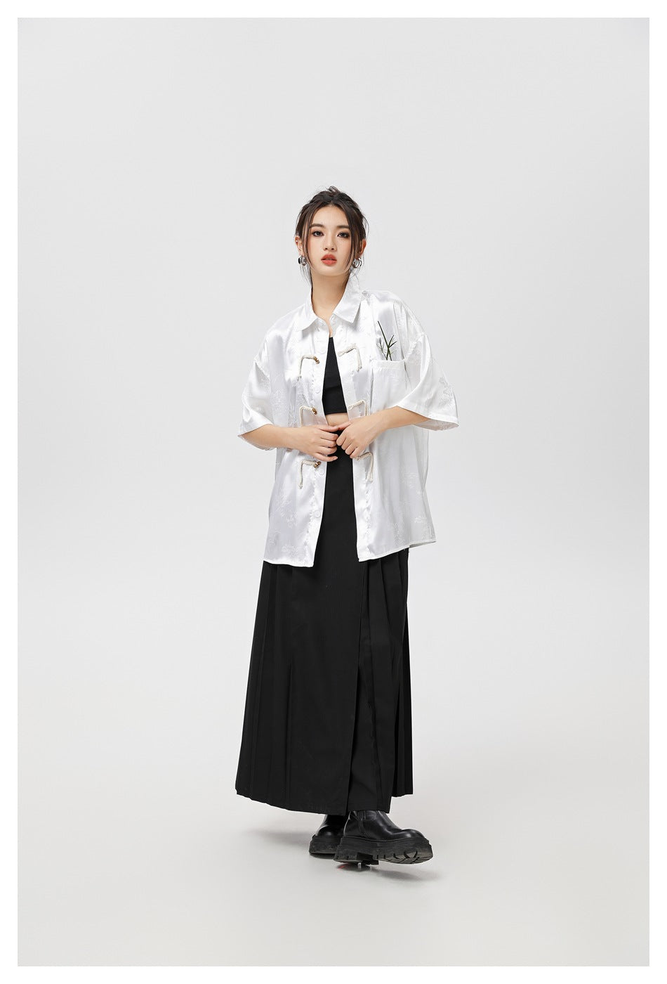 Model wearing a white patterned short-sleeve shirt with frog closures over a black outfit.