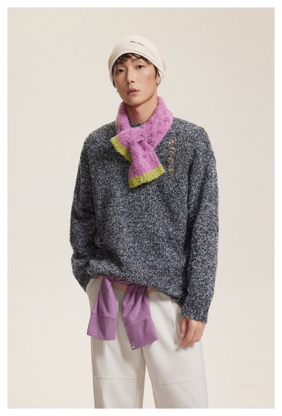 Model wearing a charcoal mottled sweater with a distressed detail, a bright pink scarf and light trousers.