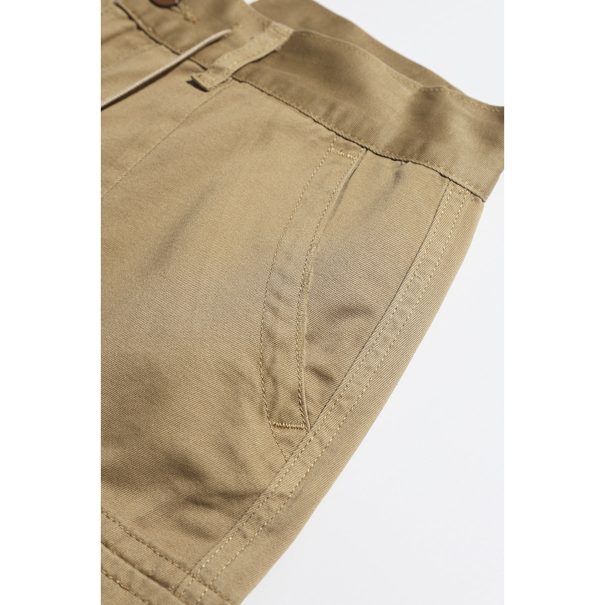 Close-up of tan shorts showing the waistband, belt loop, and curved pocket stitching.