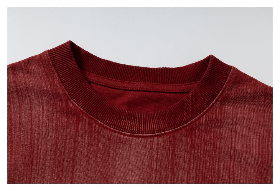 Close-up of a burgundy T-shirt's ribbed crew neckline and mottled knit surface.