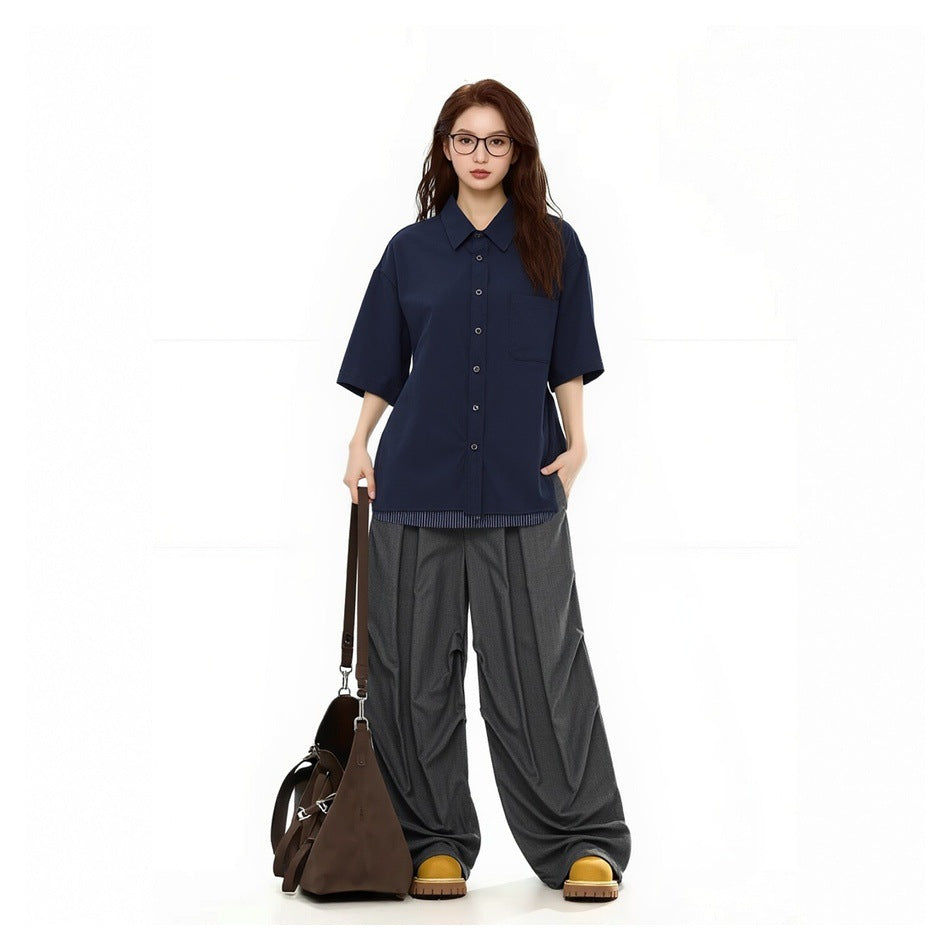 Model wearing a navy short-sleeve button-up shirt with gray wide-leg pants, yellow shoes and a brown bag