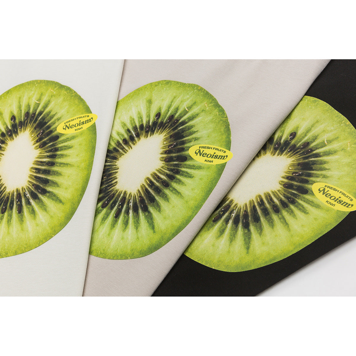 Three folded T-shirts in white, beige, and black, each with a large kiwi print.