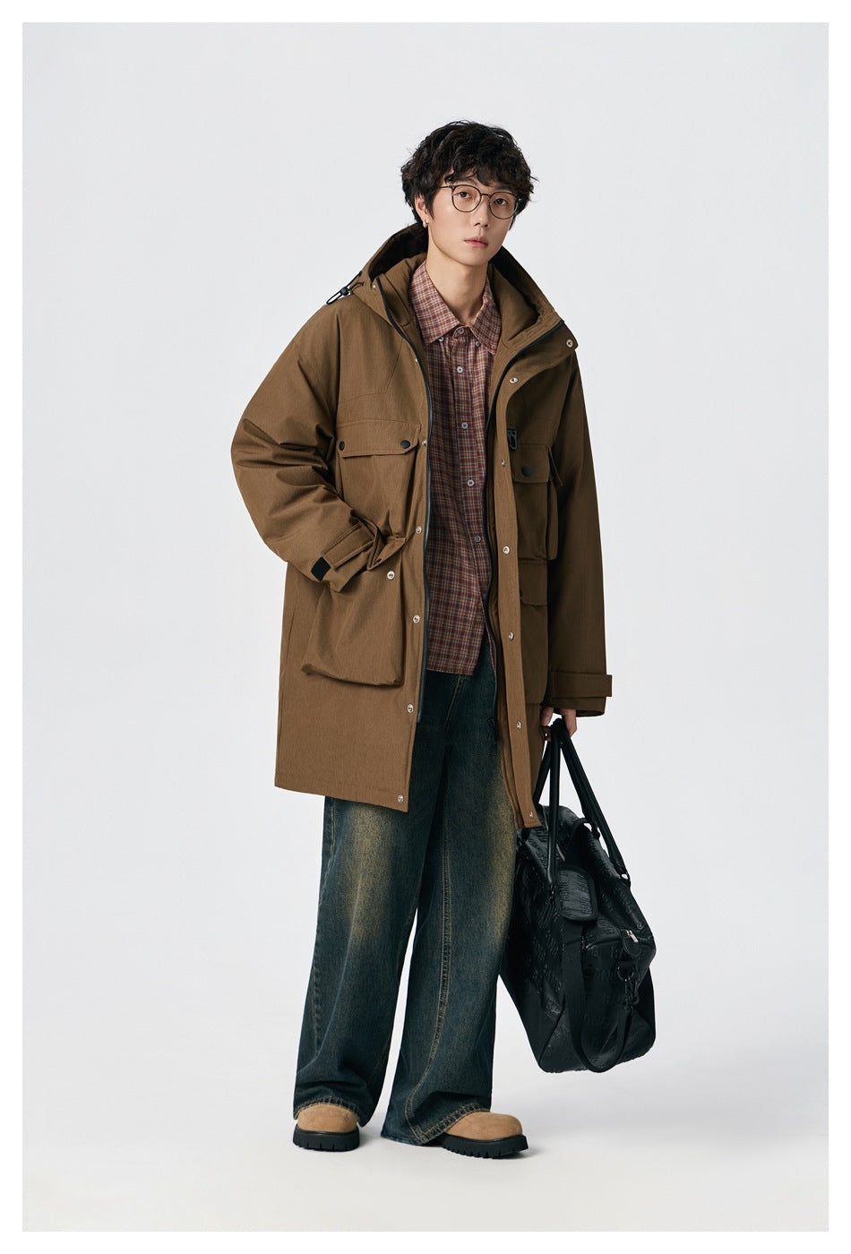 Model wearing a brown hooded long coat with large flap pockets over a plaid shirt and dark wide-leg jeans.