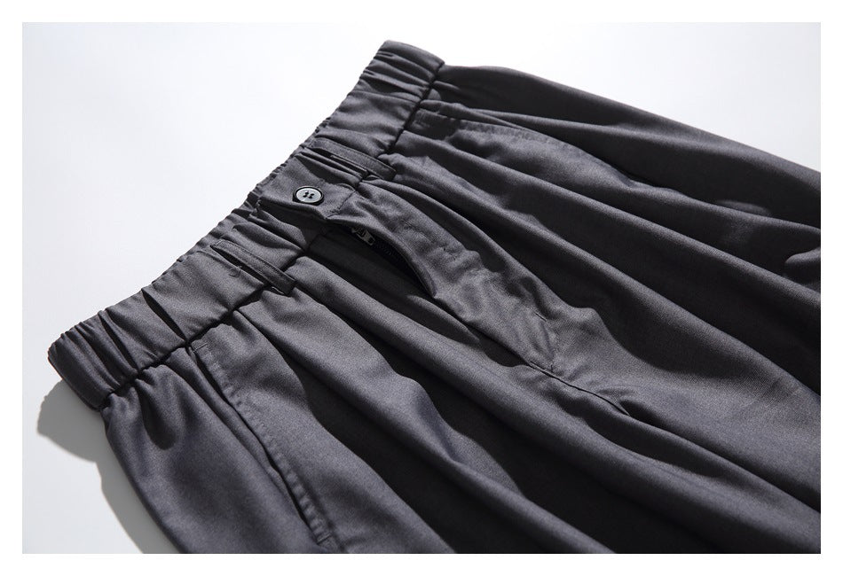 Close-up of charcoal-gray trousers showing the elastic waistband, button, fly, and front pleats.